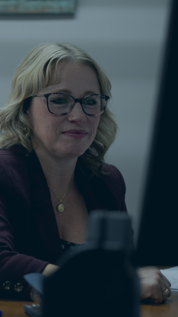 A woman wearing glasses is attentively working at her desk, surrounded by office supplies and a computer.