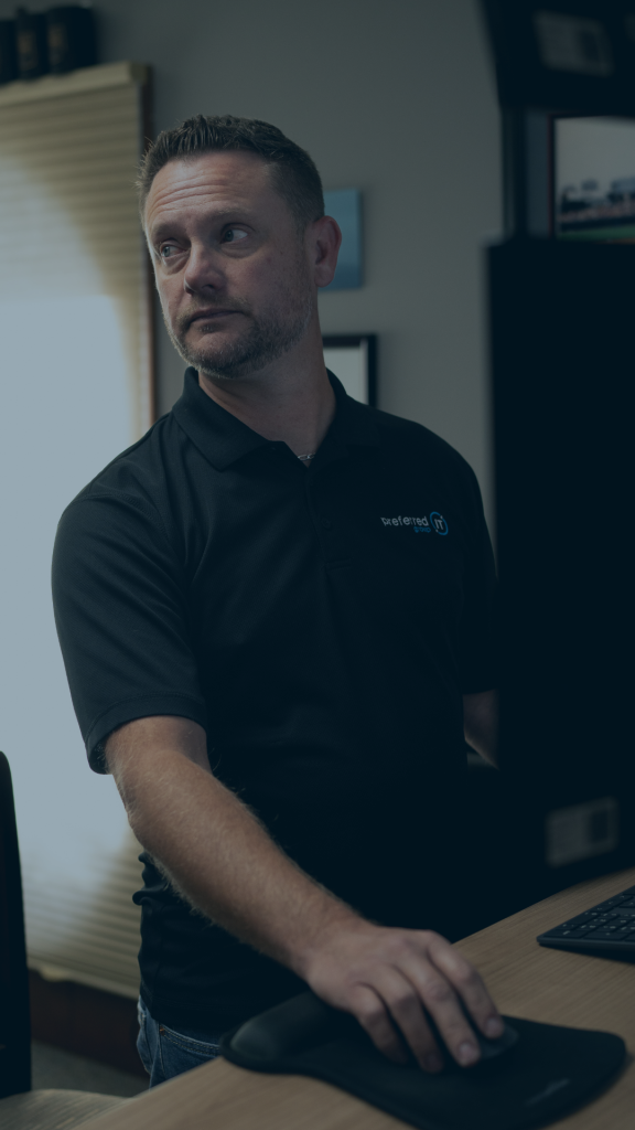 A man wearing a black shirt sits at a desk, working intently on his computer.